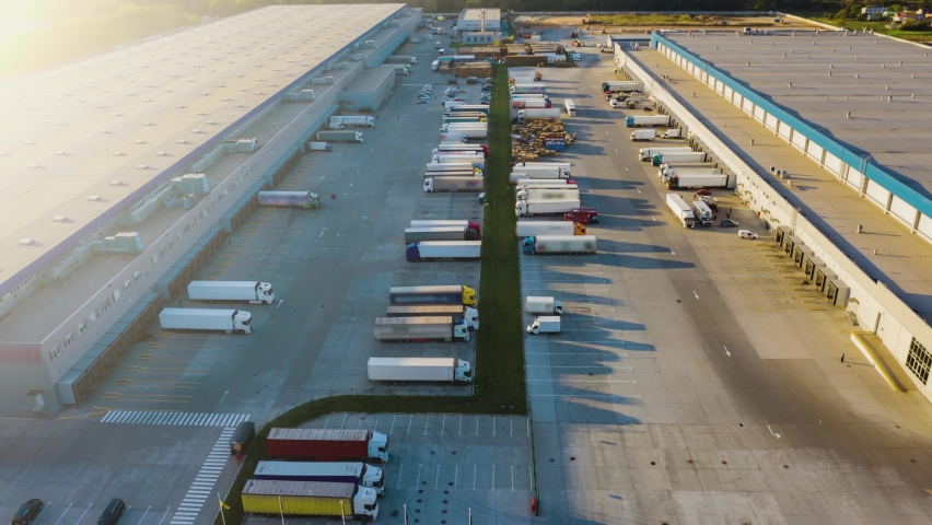 Logistics park with a warehouse - loading hub. Semi-trucks with freight trailers standing at the ramps for loading/unloading goods. Aerial hyper lapse - motion time lapse Royalty-Free Stock Footage #1061100376