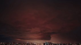 Amazing timelapse of the night storm over the big city, with colorful clouds moving on the sky and bringing first drops of rain, and bright lightnings illuminating the scene.