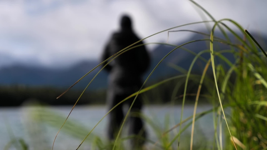 Blurry person stands alone in nature, focus on tall grass in foreground