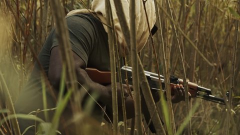 Armed Rebel Black Man Holding A Gun Walking Secretly Behind The Bush - Medium Shot