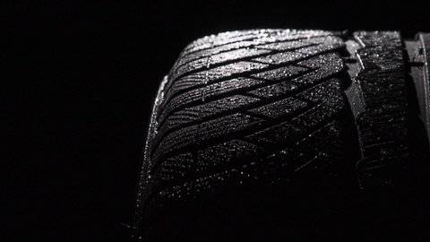 Sports Tire in Water Droplets. Loop. The geometric pattern of the wheel in water droplets slowly rotates towards the viewer. Drops sparkle on the black rubber on a black background
