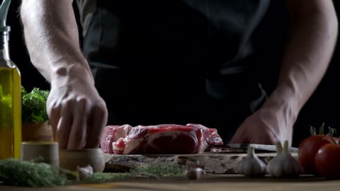 Male chefs hand sprinkling sea salt on a raw meat steak and preparing it for cooking.