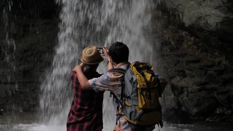 A couple with a beautiful waterfall, a couple using their smartphones to take this picture, backpacking, waterfall landscape.
