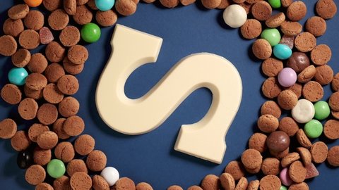 Rotation of kruidnoten, traditional sweets, strooigoed and white chocolate letter S. Background for Dutch holiday Sinterklaas. St. Nicholas day concept. FullHD video, top view