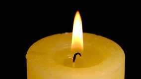 Large thick yellow candle lit and burn on a black background high resolution video clip macro shooting close-up