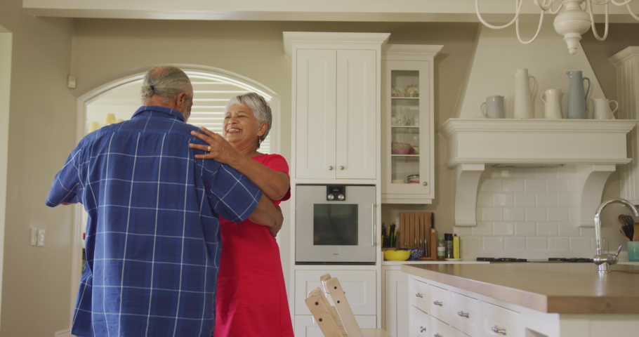 African American senior couple spending time at home together, dancing in a kitchen, looking at each other and smiling, in slow motion.