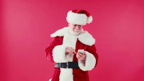 happy santa claus chatting on smartphone and touching eyeglasses isolated on red
