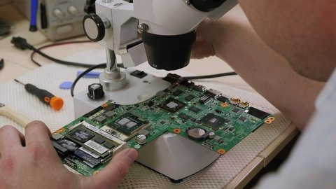 Young man repairing computer components in service center with the help of a Microscope. Electronics repair service concept.