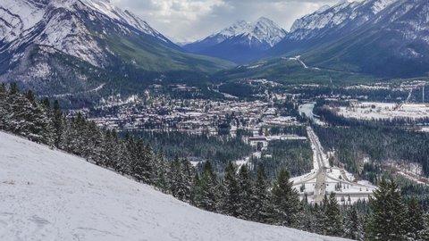 Town of Banff in snowy winter season. Snow Capped Mount Rundle, Sulphur Mountain in background. View from Mount Norquay Banff View Point. Banff National Park, Alberta, Canada. 4K Time-lapse zoom out.