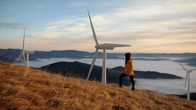 Epic shot of a woman hiking on the edge of the mountain against landscape with wind turbine power station on background. Concept of environmental engineering, renewable energy and love for nature. - Powered by Shutterstock - Get 15% off with code: PIKWIZARD15