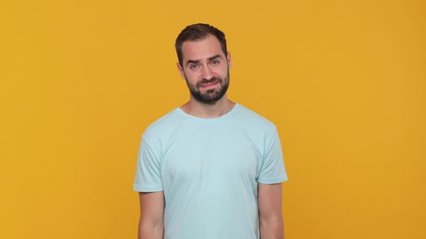 Bearded fun confused young man 20s in basic casual blue t-shirt isolated on yellow background studio. People sincere emotions lifestyle concept. Looking at camera spreading hands say oops i am sorry