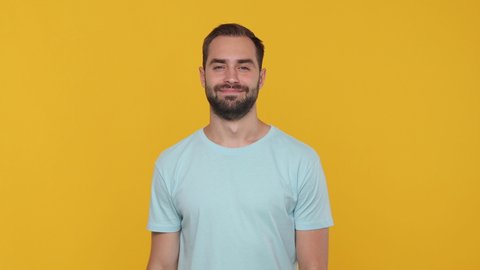 Bearded young man 20s in basic casual blue t-shirt isolated on yellow background studio. People emotions lifestyle concept. Looking camera rubbing fingers showing cash gesture asking for give me money