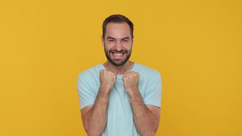 Bearded happy young man 20s in basic casual blue t-shirt looking shocked surprised wow showing hands brain explosion head isolated on yellow background studio. People sincere emotion lifestyle concept