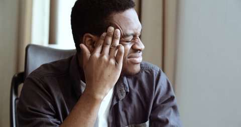 Portrait of tired african american office worker student boss suffering from headache. Stressed black man in shirt feeling pain and massaging head to relax and reduce ache indoor, close up headshot