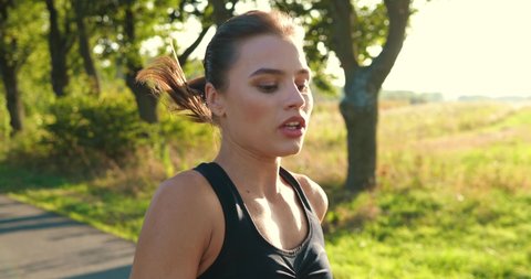 Close up portrait of young beautiful woman athlete running on road and working out on sunny day. Caucasian pretty concentrated fit sporty female training and jogging outdoors. Fitness concept