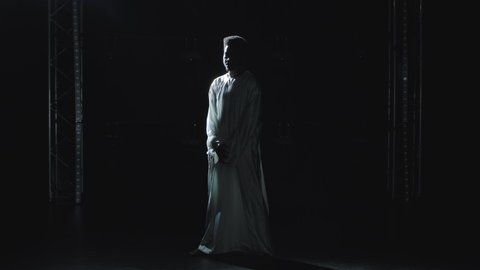 A young African American man in a white hoodie looks at the beam of light in dismay and says wow with a shocked expression on his face. Picture taken in the studio on a black background.