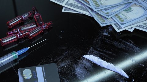 Addicted man is using drugs through rolled US dollar bill. Male sniffs cocaine white powder drug using dollar tube. Addict takes dose of drugs. Cocaine being snorted off glass surface with straw