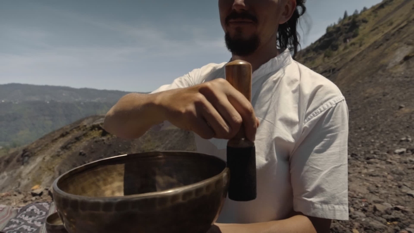 A young Asian guy playing on Tibetan singing copper cups on a viewing mountain in nature