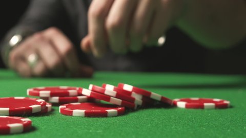 Slow motion of a male hand betting with red chips on the green poker table in casino. Close-up.