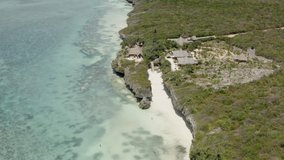 Aerial shot of Zanzibar Tanzania. Drone video of a beautiful blue ocean waves crashing against a beach of yellow sand and a rocky shore on which stand African houses surrounded by jungles.