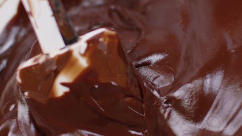 Close-up dark smoothy delicious melted chocolate stirring mixing with spatula, making hand-crafted homemade chocolate swirl - chocolate factory, confectionery production, bakery, pastry, slow motion