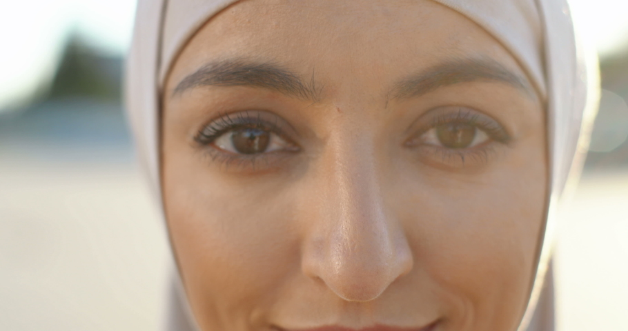 Close up of face of young muslim beautiful woman in traditional headscarf smiling happily to camera. Portrait of pretty Arabian female at street. Outdoors. Islamic girl. Charming eyes. | Shutterstock HD Video #1061140222