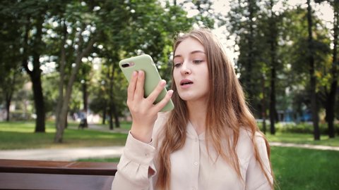 Lady sending audio voice message on smart phone at outdoor talking to mobile assistant. Girl using smartphone voice recognition, dictation message voice
