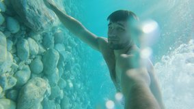 Handsome young man swimming under the water surface in turquoise blue sea at warm sunny summer
