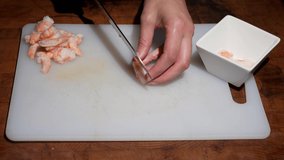 This video shows anonymous chef hands cutting seafood shrimp with a kitchen knife on a cutting board.