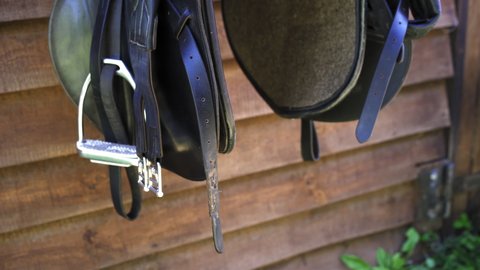 Horse equipment hangs at the entrance to the stables. Black saddle and leather aspiring. High quality 4k footage. 