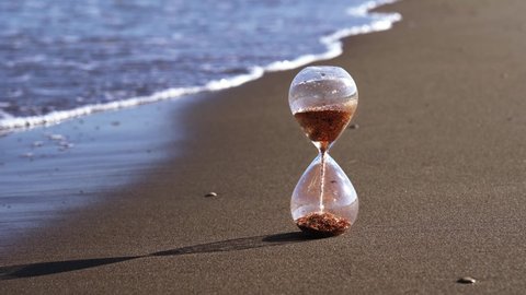 Golden sand falls in glass clock on yellow beach against sea