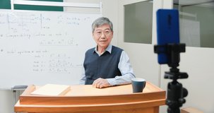 Asian mature male professor teach Engineering online through mobile phone in classroom at graduate school