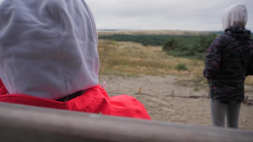 Beautiful sandy dunes reveal through the side of young and beautiful woman with a hoodie in a cold autumn day in Lithuania, Nida. Two female friends are admiring sandy dunes of Nida.
