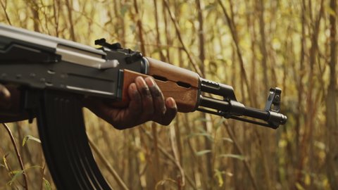 African Man Holding A Long Airsoft Electric Rifle Walking Quietly Hiding In The Woods - Closeup Shot