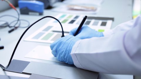Hands with blue gloves on a laboratory desk, imprints the color code on plastic board. Paint and powder factory laboratory process with color charts and industrial equipments.  