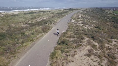 Aerial view of a woman with a bicycle by the sea in the Netherlands. The sea with waves in the background. The woman is dressed warmly. Ouddorp in the south of the Netherlands.