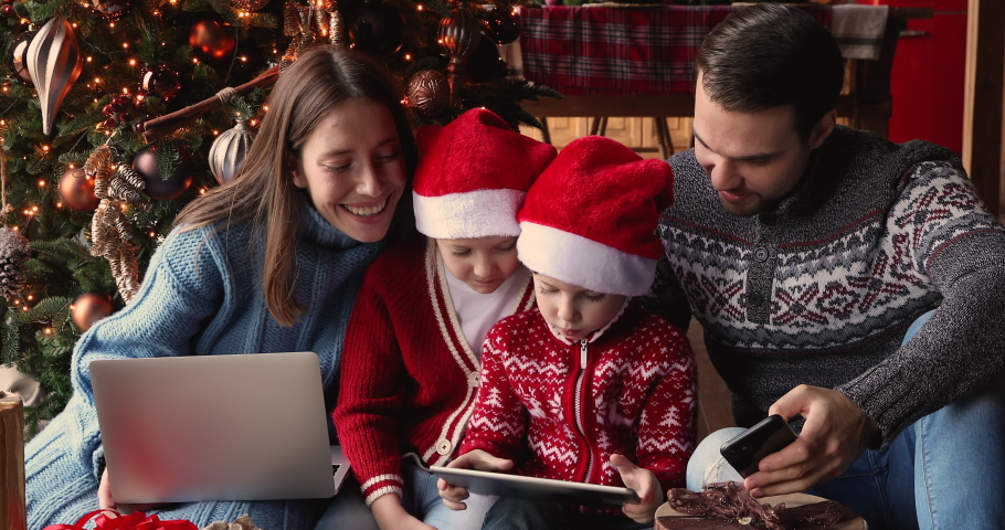 Family with small kids gathered at home near glowing Christmas tree spend holidays time using diverse electronic devices. Overuse, parental control, New Year celebration, gifts purchase online concept Royalty-Free Stock Footage #1061161819