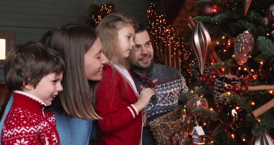 Full european family preparing for New Year winter holidays celebration concept. Married couple their daughter and son hanging spruce twigs ornaments decorating glowing twinkle light Christmas tree Royalty-Free Stock Footage #1061161855