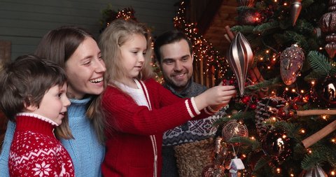 Full european family preparing for New Year winter holidays celebration concept. Married couple their daughter and son hanging spruce twigs ornaments decorating glowing twinkle light Christmas tree