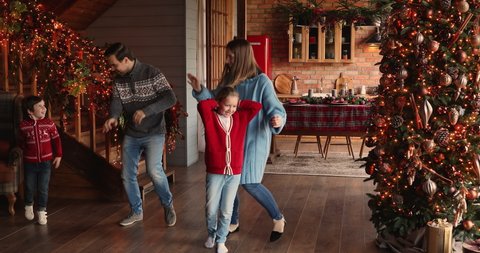 Happy active homeowners family with little children dancing at decorated bright twinkle light and glowing xmas tree home celebrate Christmas Eve. Fun with kids during New Year winter holiday concept