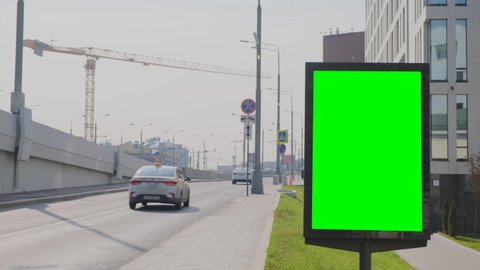 Green screen billboard located on a busy street. Cars are moving. Working day morning. People walk on the sidewalk