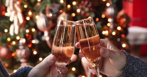 Happy couple clink champagne glasses toast and celebrate together New 2021 Year at home standing against glowing Christmas tree bright bokeh background, close up hands view. Congratulations concept Stockvideó