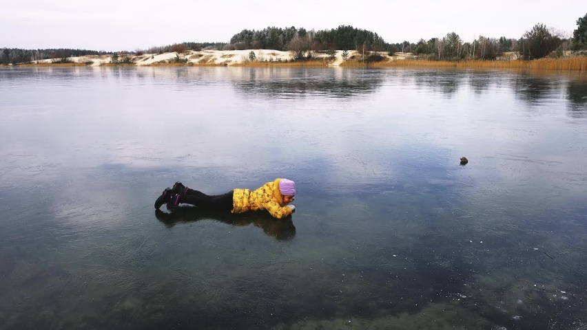 Little girl in the yellow jacket crawling on a slippery frozen lake.