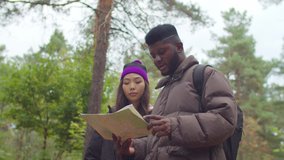 Positive beautiful multiethnic hiking couple with backpacks reading travel map, navigating and looking for directions in autumn forest while backpacking together during active lifestyle vacations. - Powered by Shutterstock - Get 15% off with code: PIKWIZARD15