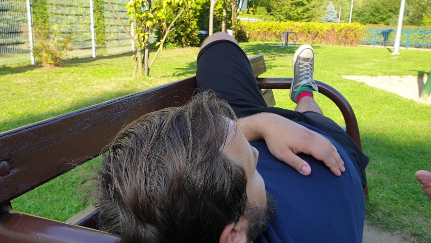Tired parent laying down on a bench in the playground