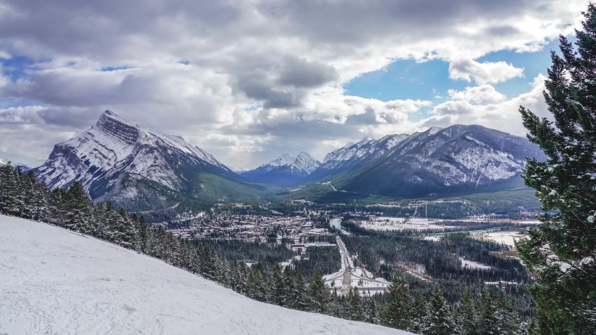 Town of Banff in snowy winter season. Snow Capped Mount Rundle, Sulphur Mountain in background. View from Mount Norquay Banff View Point. Banff National Park, Alberta, Canada. 4K Time lapse zoom in.