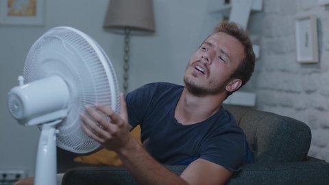 Man suffering from the summer heat and trying to cool off with her fan. A sweaty woman is disturbed by the air conditioner malfunction in the humidity concept.