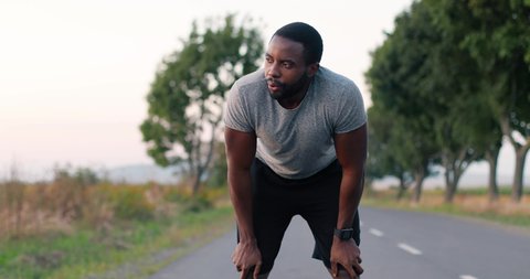 Young African American tired sweaty man jogger stop in running and breathing difficult on road in countryside. Male runner in sweat loosing breath in jogging.