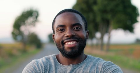Close up of African American handsome male jogger standing on road in countryside on summer day, crossing hands and smiling. Sporty man jogging outside. Sport. Portrait of sportsman runner.