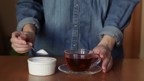 Woman hand adding a lot of sugar in a coffee from a sugar bowl, suggesting sugar overdose or an unhealthy diet concept.